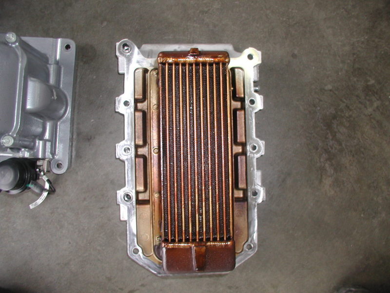 Copper supercharger intercooler core removed from an aluminum intake manifold on a shop floor