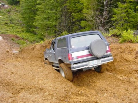 1989 Ford Bronco - This Ford Bronco is navigating a muddy trail, with its rear end angled upwards on the incline.