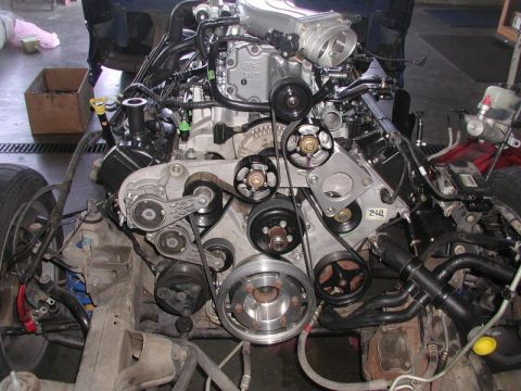 2007 Ford Mustang - Close-up view of a Ford V8 engine, showing the supercharger, belts, and pulleys in a workshop setting.