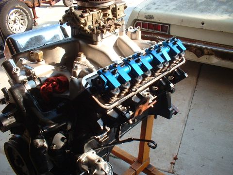 1957 Ford Custom Sedan - Close-up of a car engine on a stand, with a portion of a white vehicle in the background.