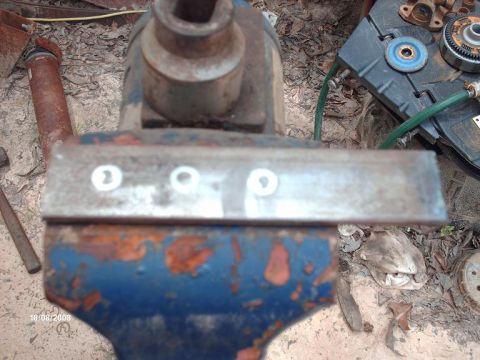 1990 Ford F-150 - A metal bar is secured in a vise, with various mechanical parts scattered around the work area.