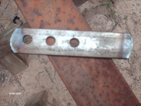1990 Ford F-150 - A close-up view of a metal bracket with three circular holes, positioned on a rusty surface.
