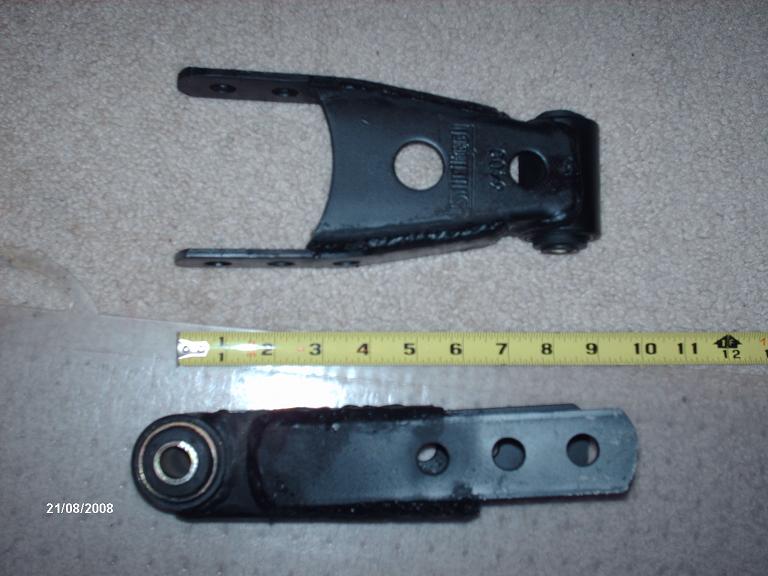 Two black metal suspension components, one with a measuring tape showing inches