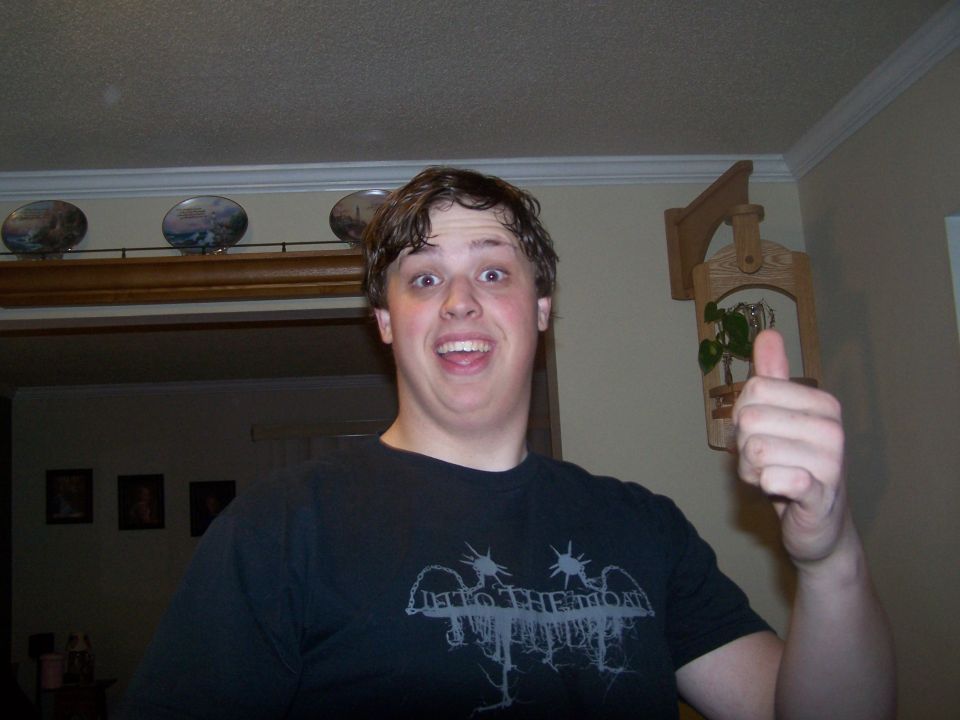 guy with surprised expression gives a thumbs up, wearing a black t-shirt with a band logo