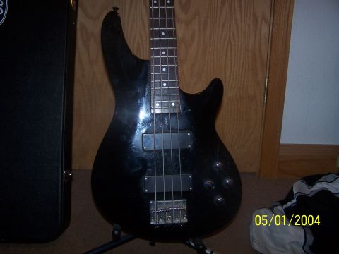 1979 Ford Bronco - A black electric bass guitar is shown on a stand with a case to the left and a wooden door in the background.