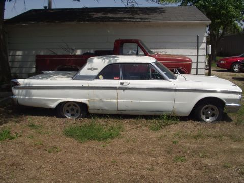 1979 Ford Bronco - A white coupe sits parked in front of a garage with a red pickup truck behind it.