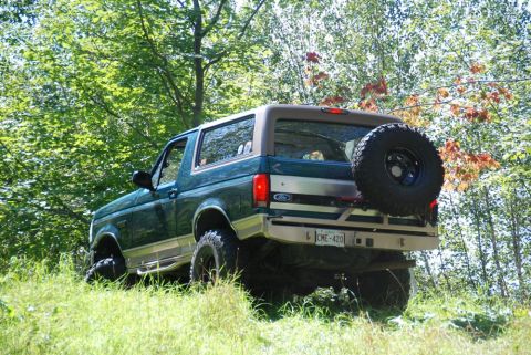 1996 Ford Bronco - Rear view of a 1996 Ford Bronco parked on a grassy incline surrounded by trees.