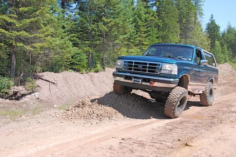 1996 Ford Bronco - A teal Ford Bronco navigates a rough dirt path, its off-road capabilities.