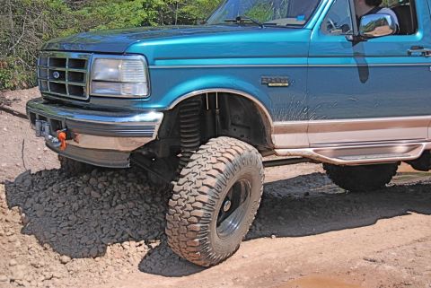 1996 Ford Bronco - Teal Ford Bronco with lifted suspension and off-road tires navigates a rough, gravelly terrain.