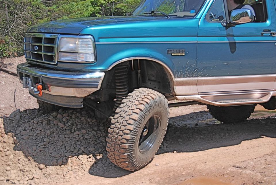 Teal Ford Bronco with chrome bumper and winch, lifted suspension, off-road tires, on gravel
