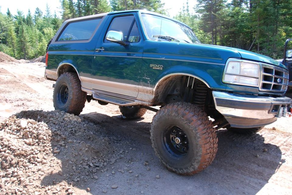 Teal 1996 Ford Bronco with lifted suspension and off-road tires on a dirt road