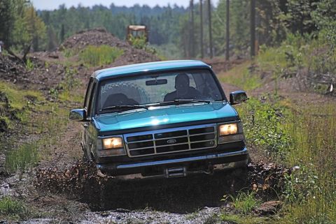 1996 Ford Bronco - A green 1996 Ford Bronco navigates a muddy trail with trees and debris in the background.