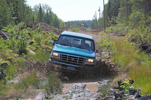 1996 Ford Bronco - This teal SUV navigates a muddy trail, kicking up water and dirt.