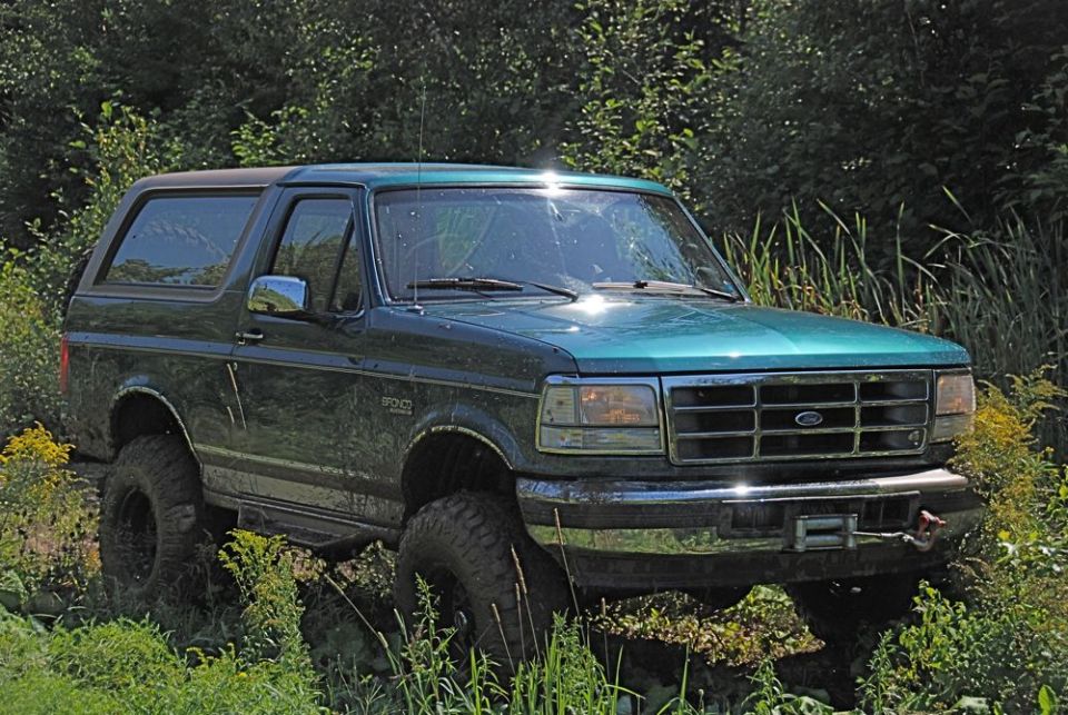 Green 1996 Ford Bronco with lifted suspension and off-road tires parked in tall grass