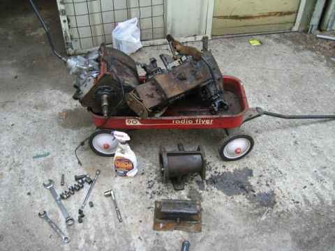 1995 Ford Bronco - Various automotive drivetrain components are staged on a concrete surface next to a child's wagon.