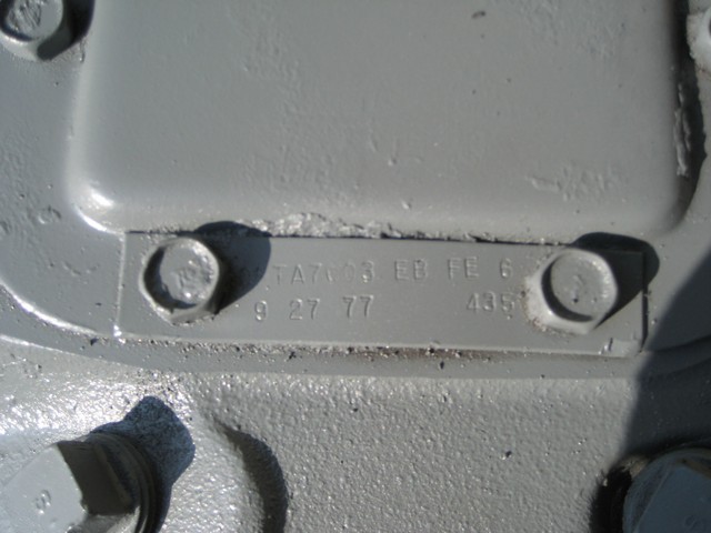 Close-up of a metal data plate with stamped text on a gray painted surface.