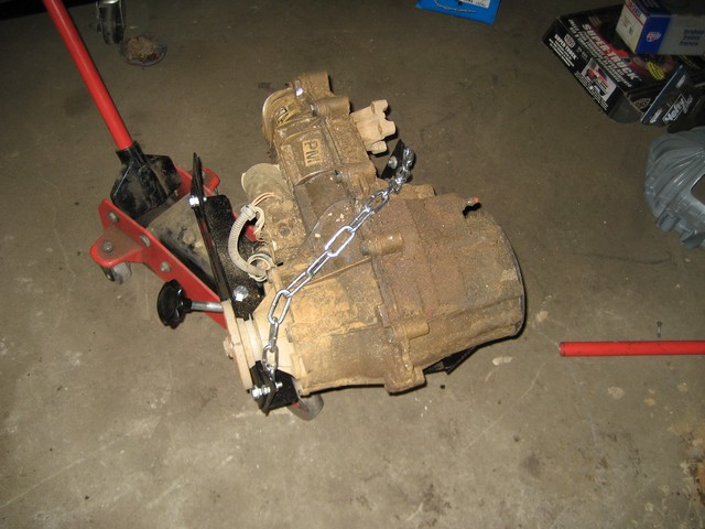 Transfer case on a red hydraulic floor jack, secured with a chain.