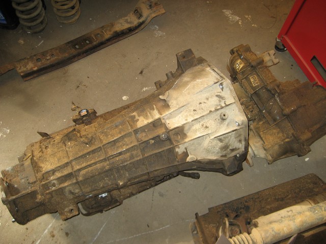 Two dirty automotive transmissions and rusty parts on a concrete floor.