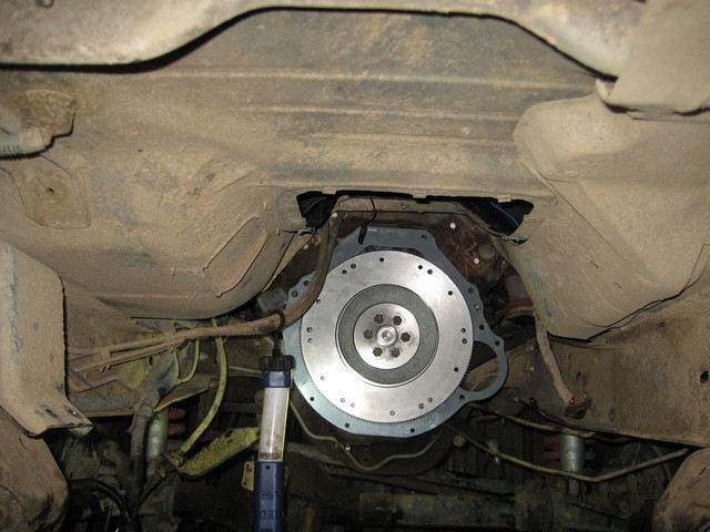 Underneath view of a vehicle showing a new flywheel and adapter plate installed.