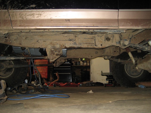 Underside of a 1995 Ford Bronco showing frame, suspension, and drivetrain in a garage.