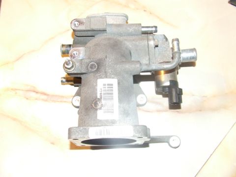 2003 Ford Crown Victoria - A gray metal throttle body assembly is shown against a marbled background. The part has various tubes, sensors, and a black electrical conn…