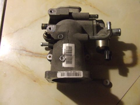 2003 Ford Crown Victoria - A close-up, overhead view of a gray automotive throttle body assembly with various tubes and a silver actuator. A white label with a barcod…