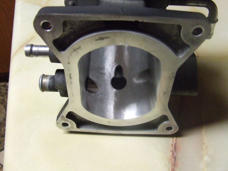 Machined metal automotive part with hose fittings, resting on a marbled surface.