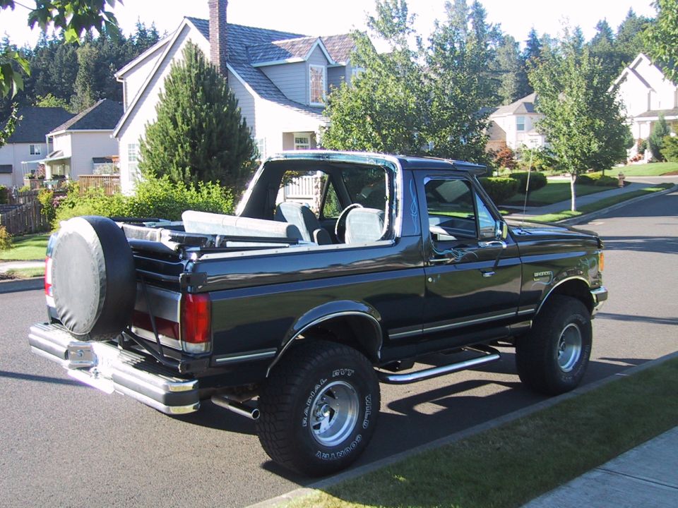 Dark full-size Ford Bronco with top removed, lifted on off-road tires, rear 3/4 view