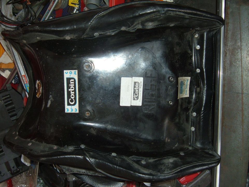 Underside of a black Corbin motorcycle seat with two stickers.