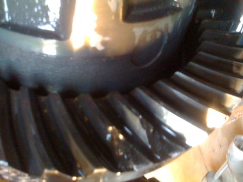1966 Ford Bronco - A close-up view shows the teeth of a large metal gear, likely a differential gear, with a reflective, dark surface. The gear is partially o…