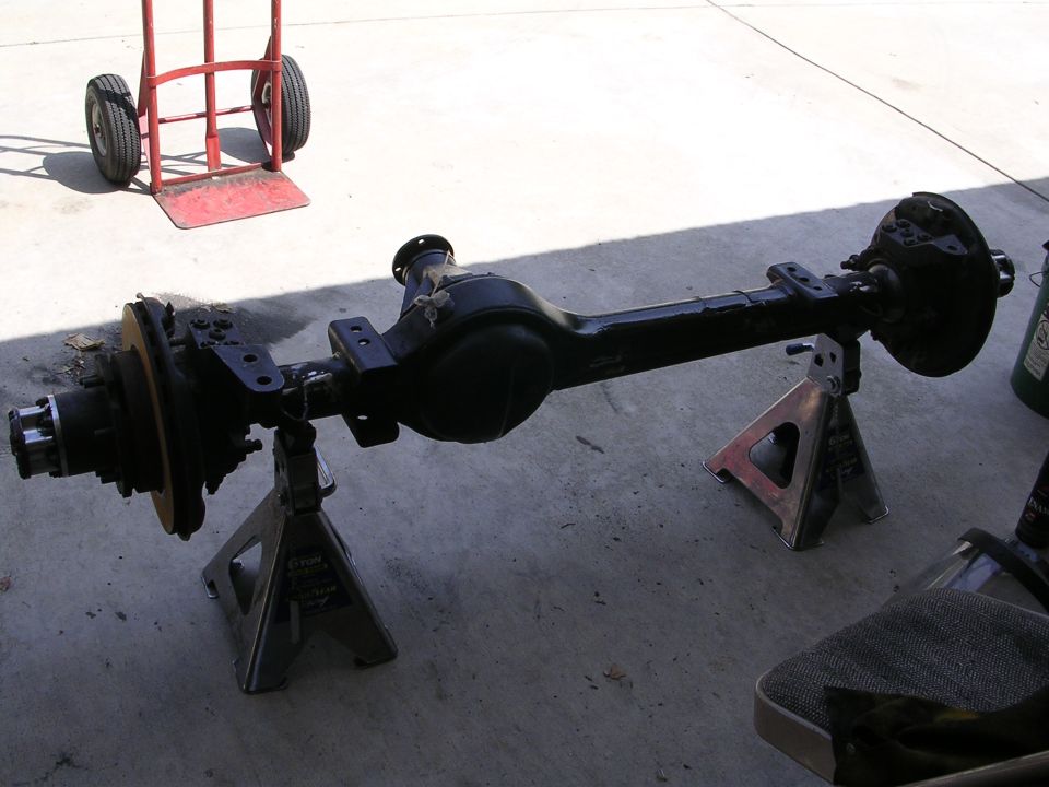 Black rear axle assembly on jack stands with a red hand truck in the background.