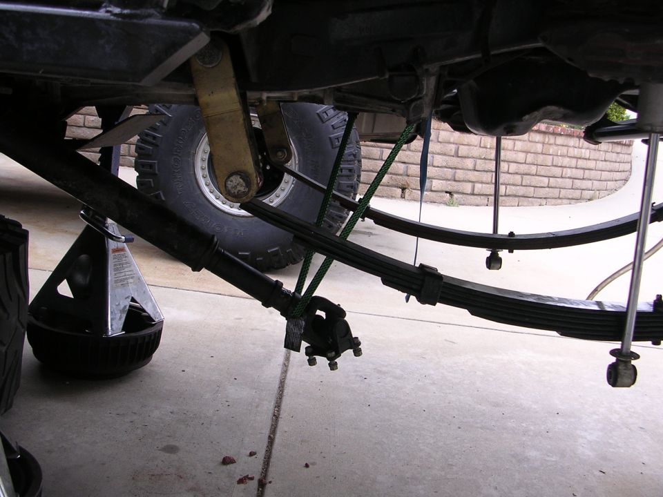 Underside of a vehicle showing leaf springs, driveshaft, and jack stand.