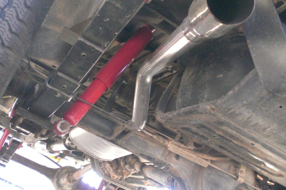 Underside of vehicle showing red shock absorber, stainless exhaust with chrome tip, muffler and rear axle