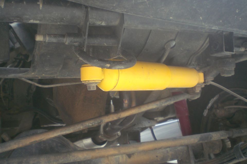 Yellow steering stabilizer shock mounted under a Suzuki Samurai, seen from below