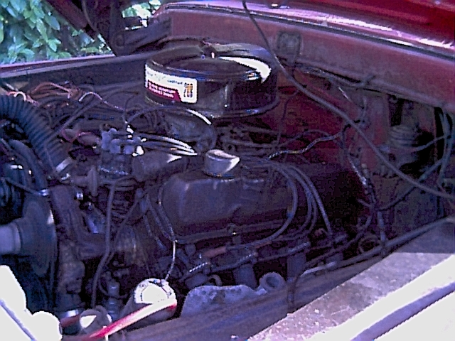 Engine bay of a dark red pickup with black round air cleaner atop an inline-six engine