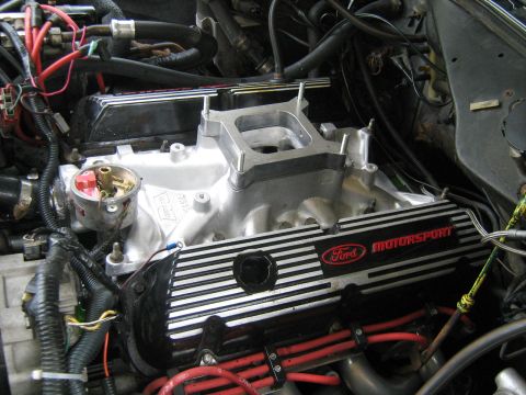 1988 Mercury Grand Marquis - A close-up view of a Ford Motorsport engine, likely a 302 V8, with a silver intake manifold and black and silver striped valve covers. Vari…