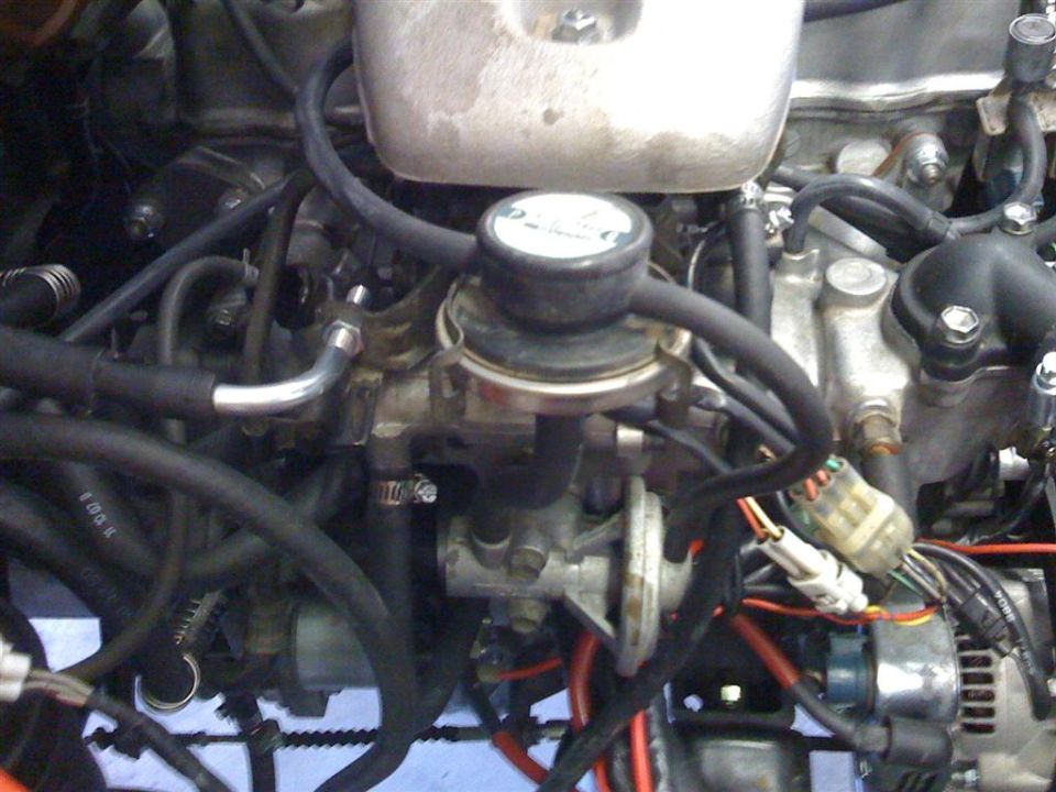 Close-up of carbureted engine top showing carburetor, vacuum hoses and wiring