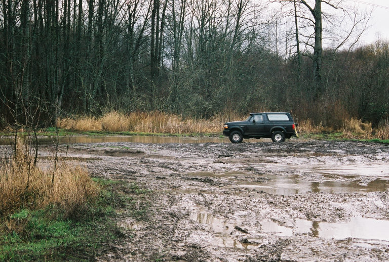 Dark Ford Bronco SUV parked in profile in a muddy field