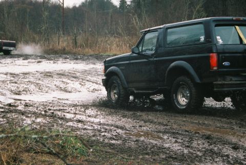 1995 Ford Bronco - A black SUV navigates a muddy terrain with another vehicle visible in the distance.