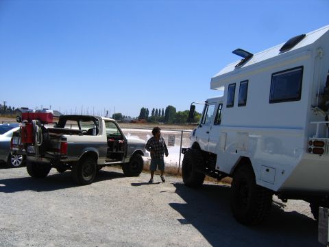 1991 Ford Bronco - A man stands between a Ford Bronco and a large, custom camper truck on a sunny day.