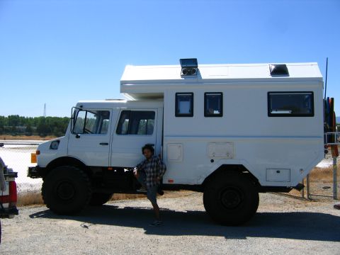 1991 Ford Bronco - A white expedition camper truck is parked outdoors with a person leaning against its side.