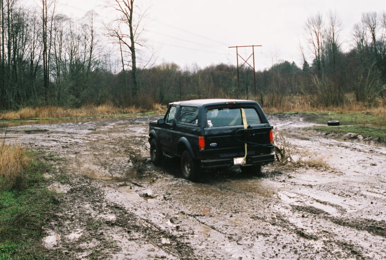 Dark Ford Bronco SUV splashing through mud from rear angle