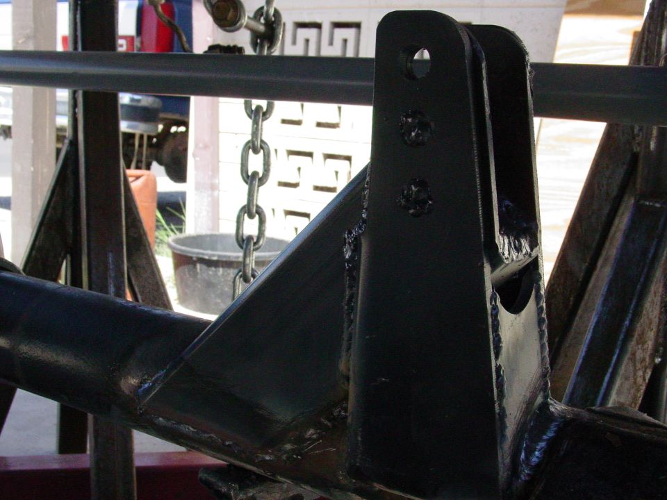 Black metal suspension part with welds and bracket, supported by stands.
