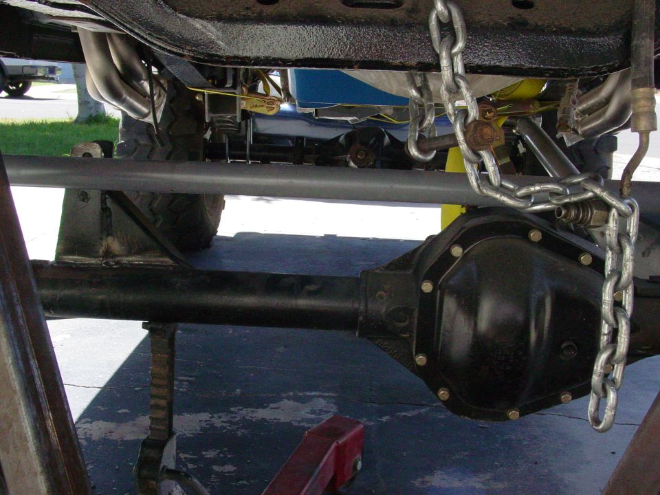 Underside of a vehicle showing rear differential, exhaust headers, and chain.