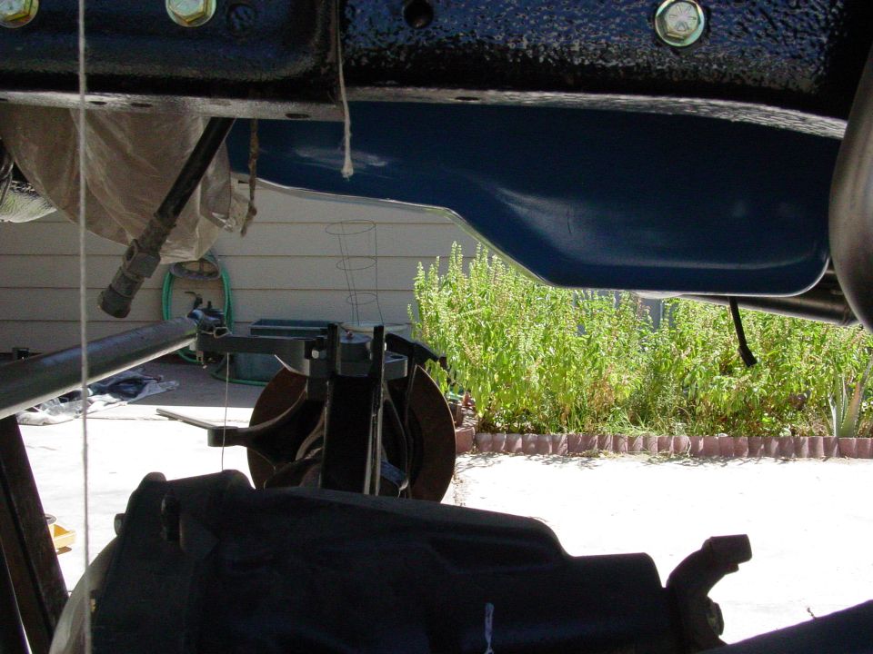 Underside of a vehicle with blue oil pan, outdoors.