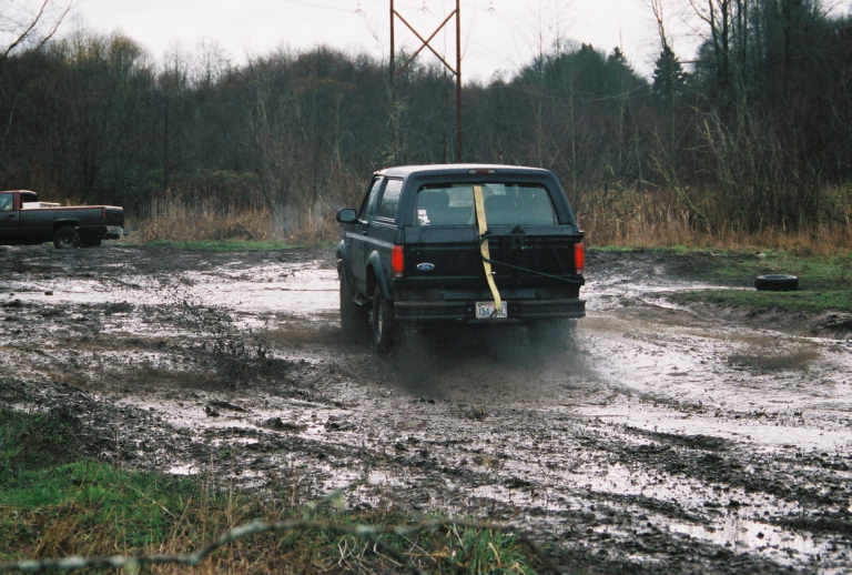 Dark Ford SUV driving through mud with rear view and yellow rear-window strap