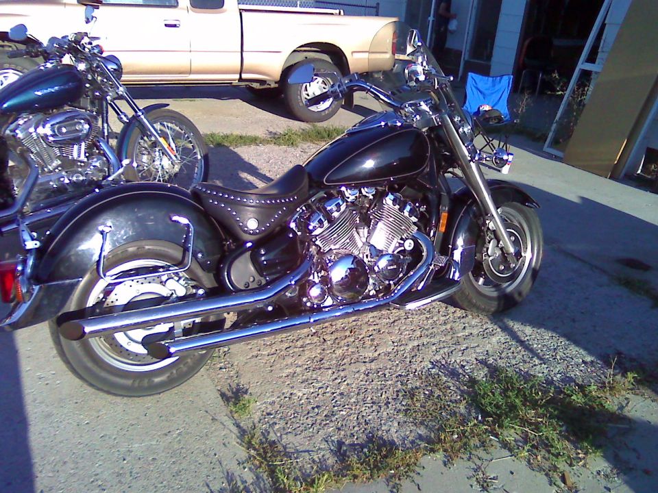 Dark blue chrome V-twin cruiser motorcycle with studded seat parked on pavement, pickup truck behind