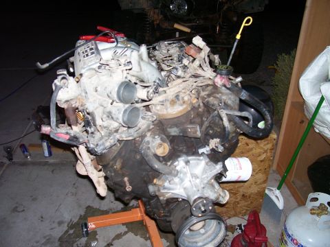 1991 Ford Bronco - A disassembled V8 engine is mounted on an orange engine stand, with various hoses, wires, and components visible. The engine is dirty and a…