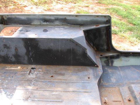 1980 Jeep CJ7 - Bare sheet-metal tub of a small SUV sitting on the ground outdoors, showing the rear wheel well, wheel arch and ribbed floor pan in strippe…