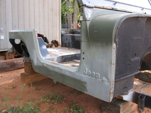 1980 Jeep CJ7 - The Jeep CJ tub and frame are shown in a primer finish, resting on wooden blocks outdoors.
